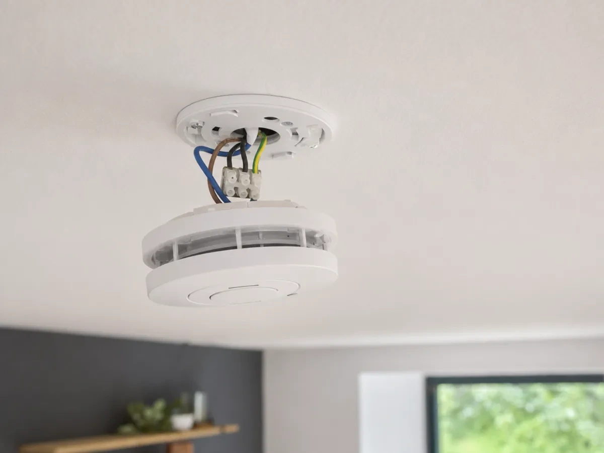 Smoke alarm being fitted to its ceiling base with the wiring connected by Re-energize Electrical