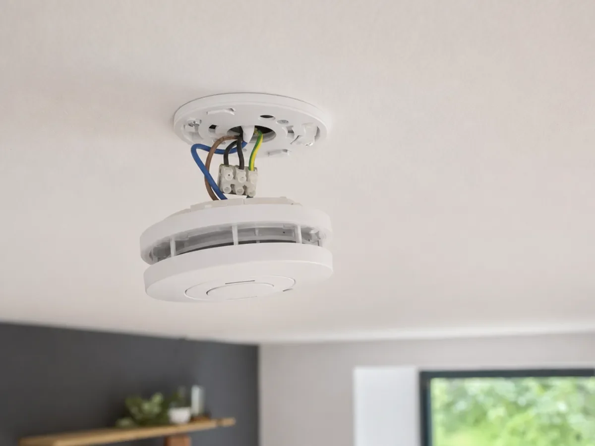 Smoke alarm being fitted to its ceiling base with the wiring connected by Re-energize Electrical